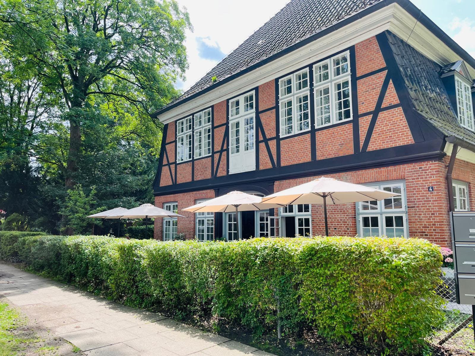 Das Stavenhagenhaus: Fachwerkfassade aus rotem Backstein mit weißen Sprossenfenstern, davor Sonnenschirme und eine Hecke