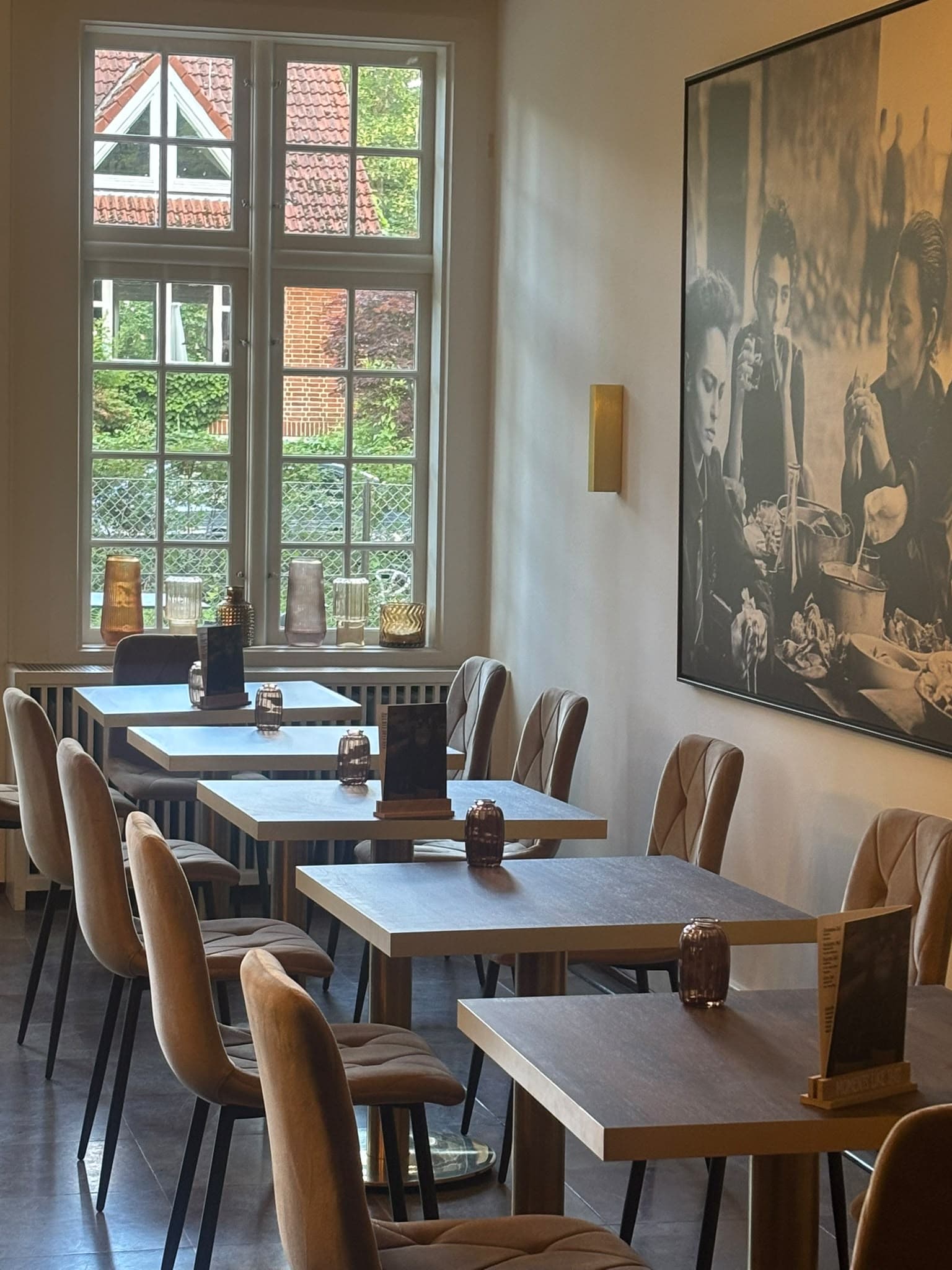 Tischreihe am Sprossenfenster mit samtbezogenen Stühlen, an der Wand ein großes Schwarzweiß-Foto