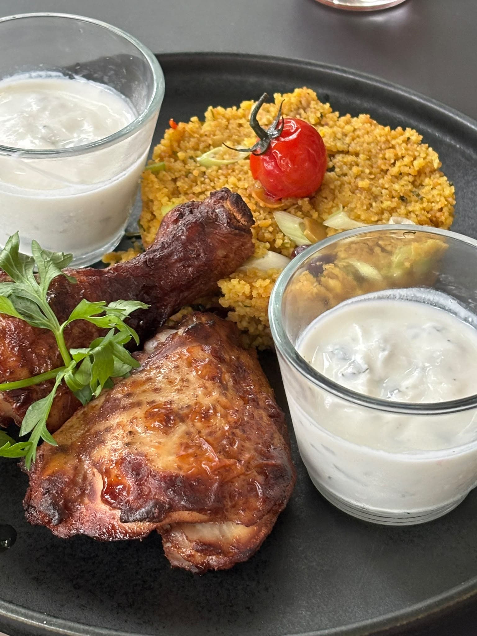 Teller mit geschmorter Hähnchenkeule, Couscous mit Kirschtomate und zwei Gläsern Joghurt-Dip
