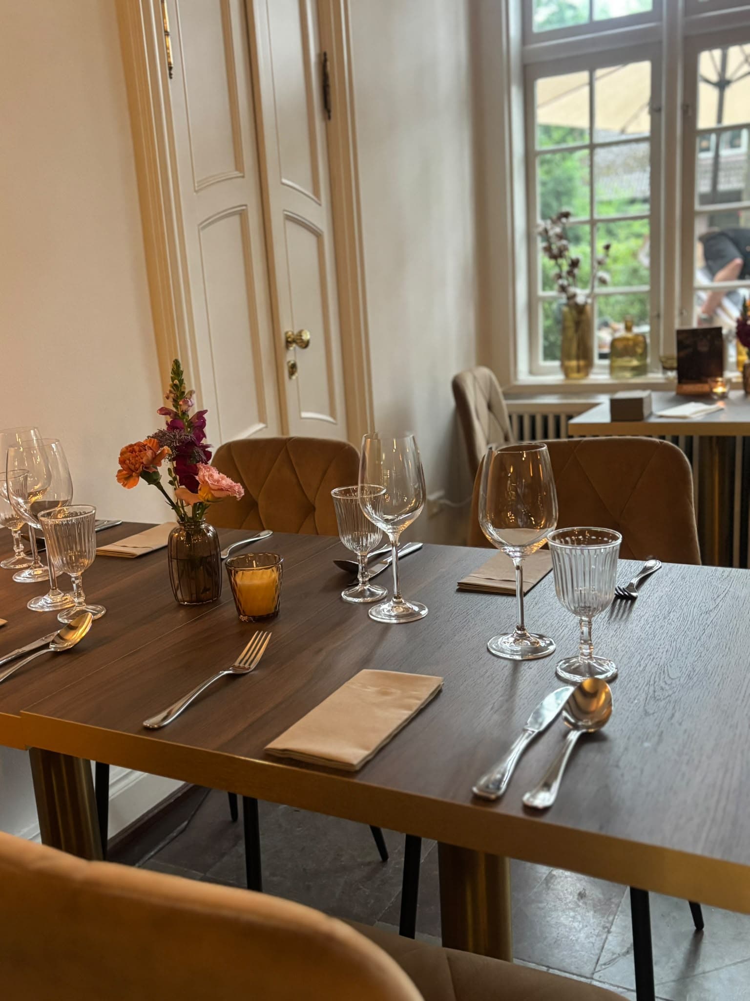 Eingedeckter Tisch mit Weingläsern, Blumen und Kerze am Fenster