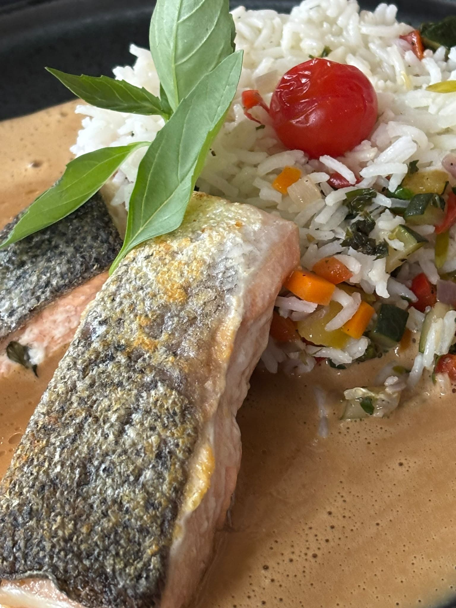 Gebratenes Fischfilet mit krosser Haut auf Gemüsereis mit Kirschtomate und Basilikum, in heller Sauce